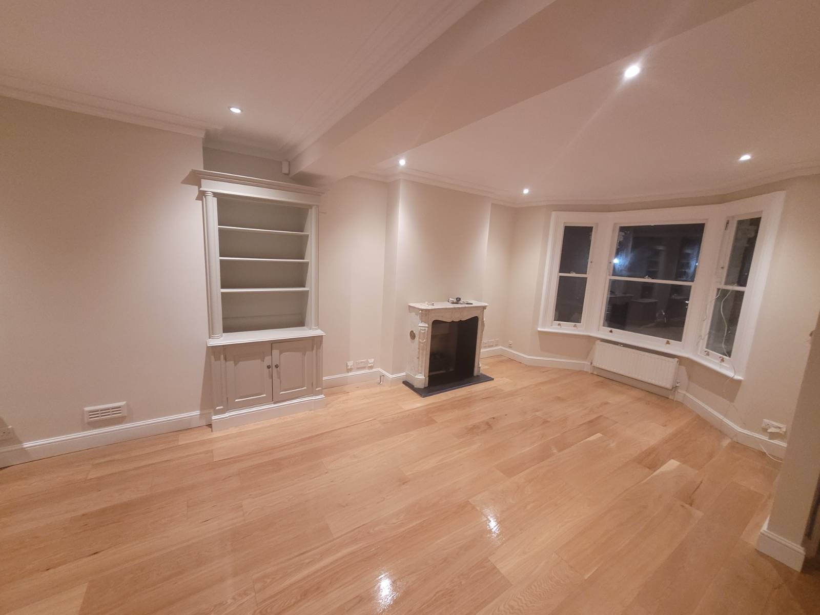 Period living room with oak flooring, alcove bookcase and bay window